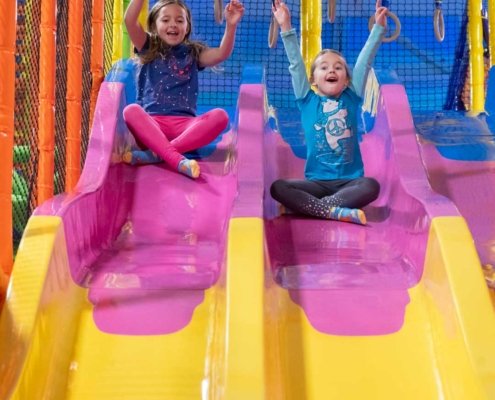 indoor-playground-slides two girls sliding down a slide at an indoor playground during birthday party